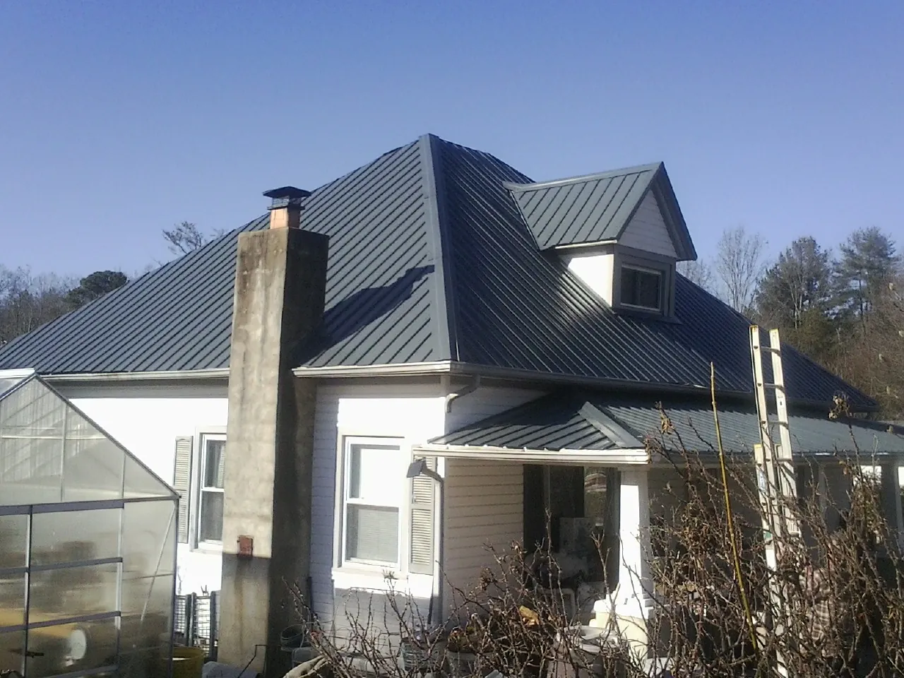 Dark blue standing seam metal roof on a white farmhouse with dormer — Slate & Tile Roof Repair by Roofing Brothers in Olmsted Falls