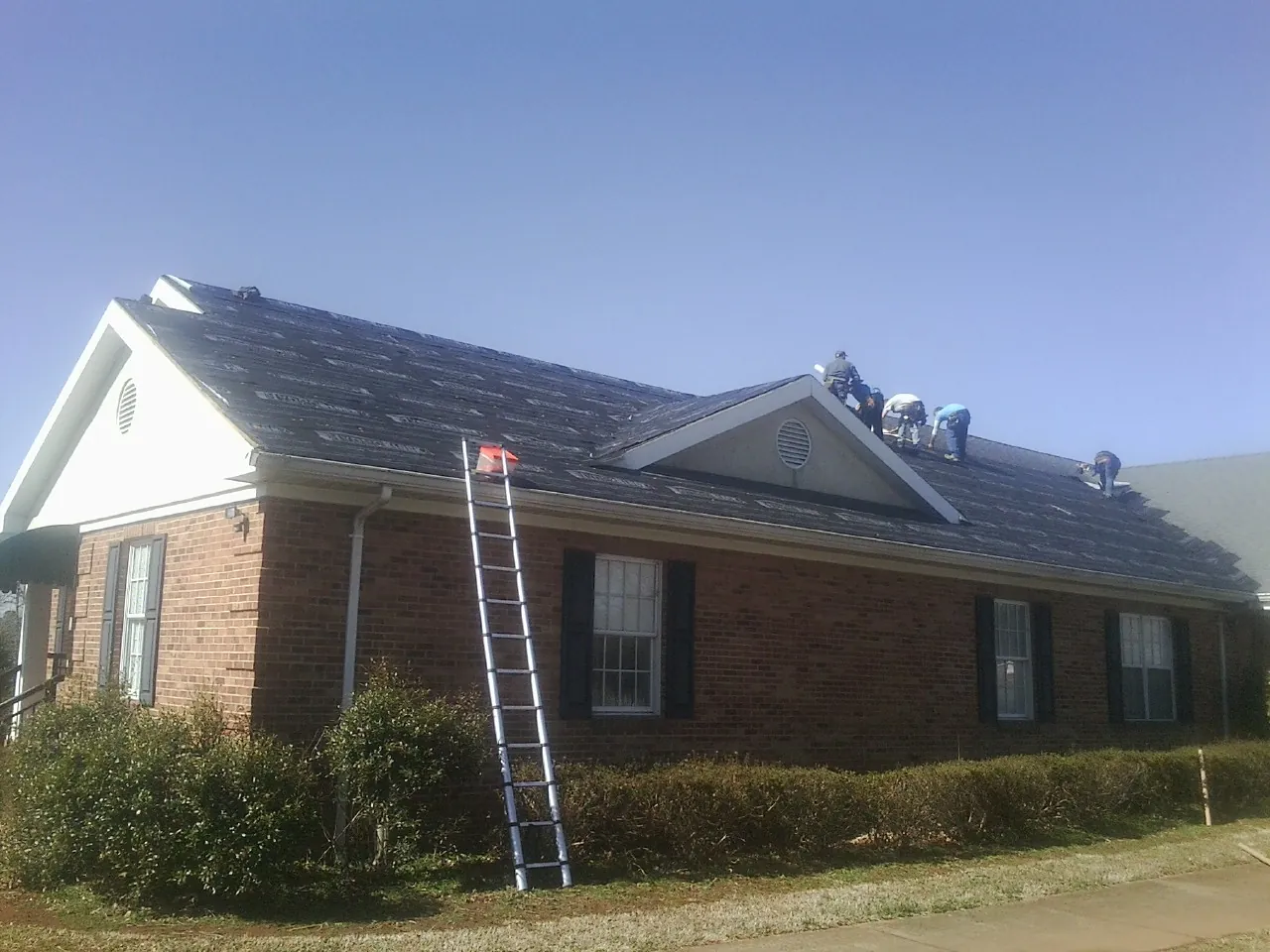 Crew tearing shingles off a brick ranch roof with a ladder set — Emergency Roof Repair work by our crew in Olmsted Falls