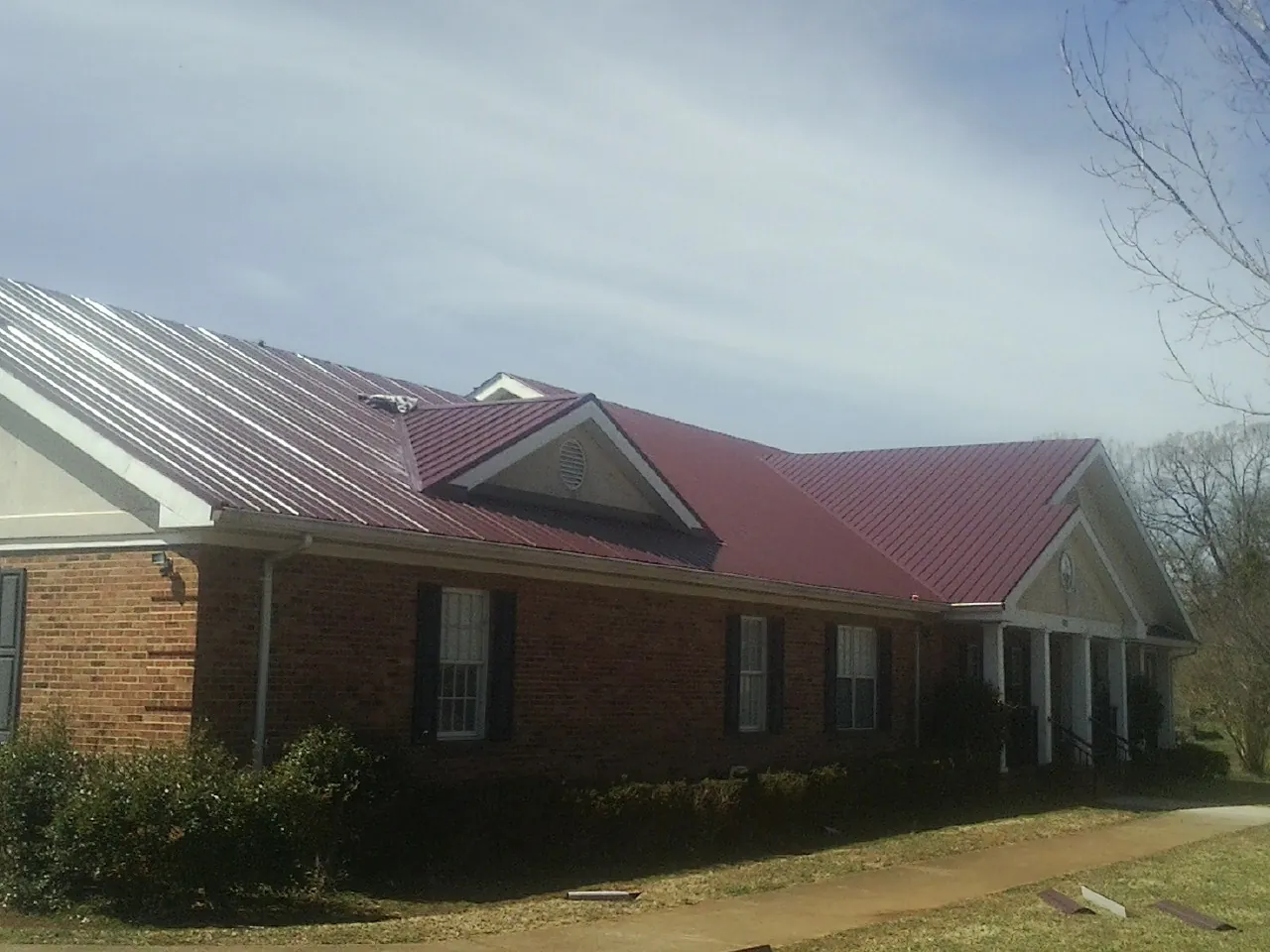 Red metal roof with gabled entries on a long brick building, from a Hail Damage Roof Repair job in Olmsted Falls