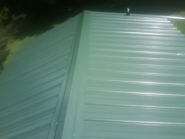 New green metal panels meeting at the ridge of a roof — Flat Roof Repair work by our crew in Olmsted Falls
