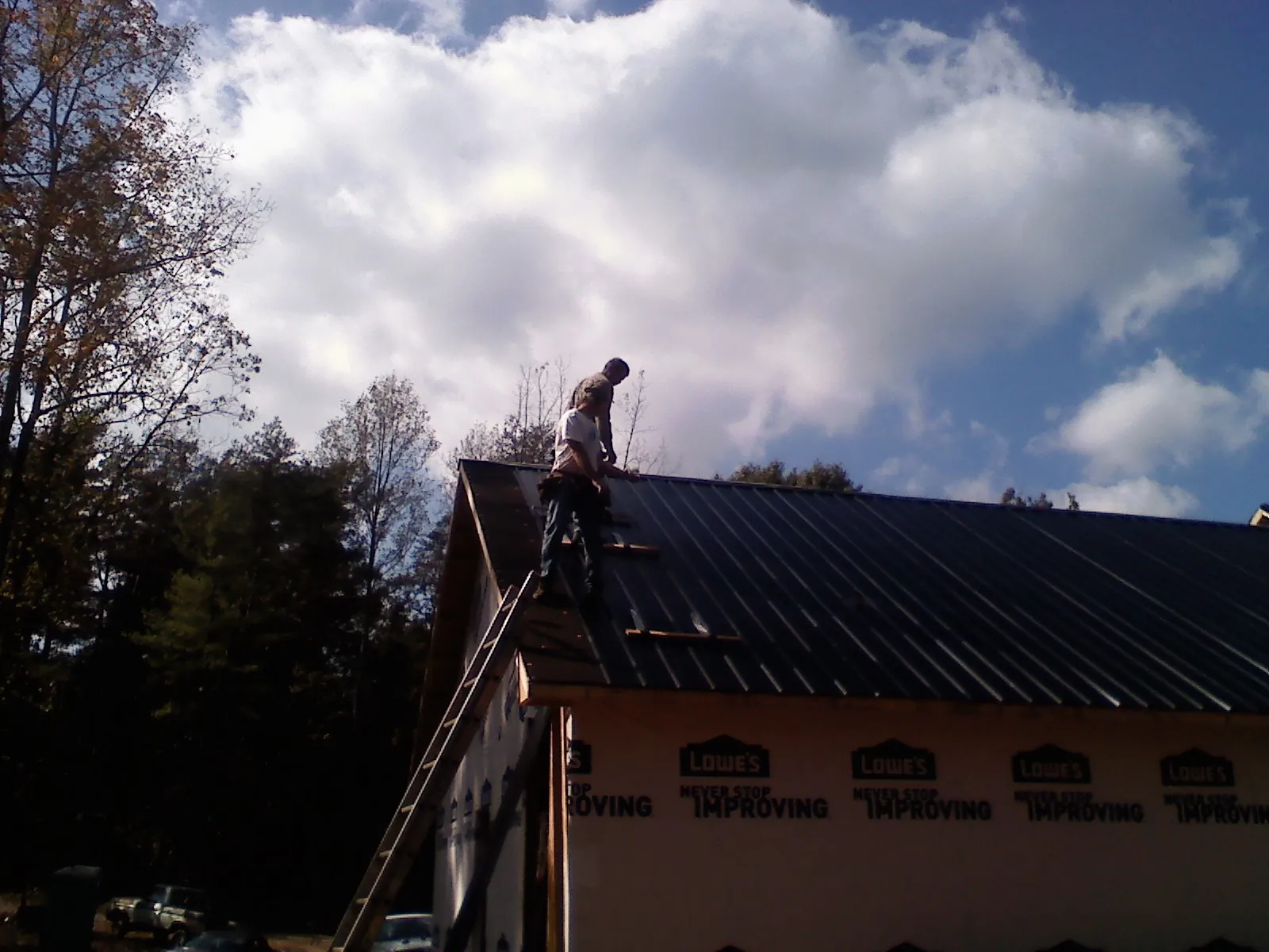 Roofer fastening dark metal panels high against a cloudy sky, from a Roof Inspection job in Olmsted Falls