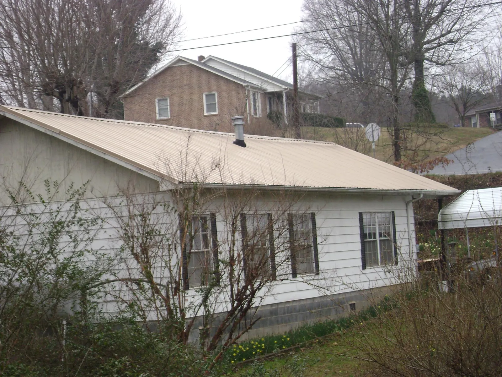 Tan metal roof on a white sided house set into a hillside — Commercial Roofing by Roofing Brothers in Olmsted Falls