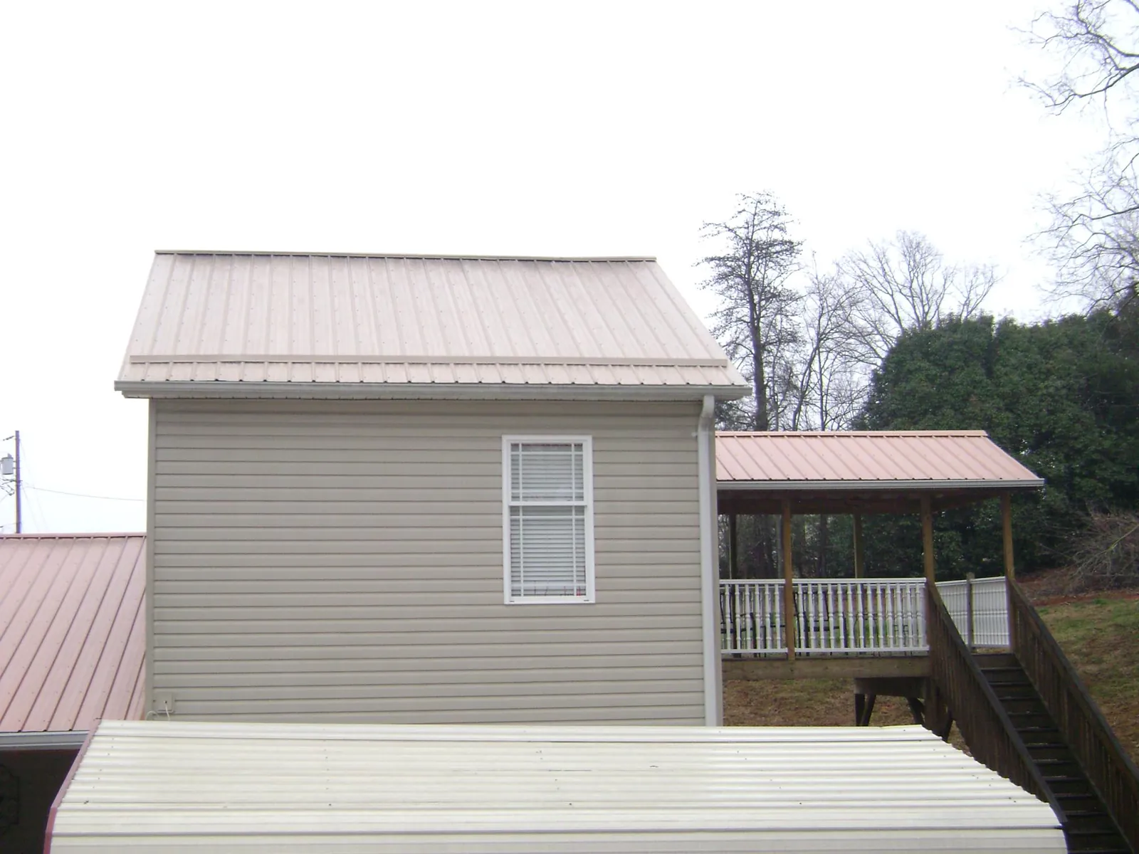 Tan metal roofs on a two story addition and attached porch, from a Roof Replacement job in Olmsted Falls